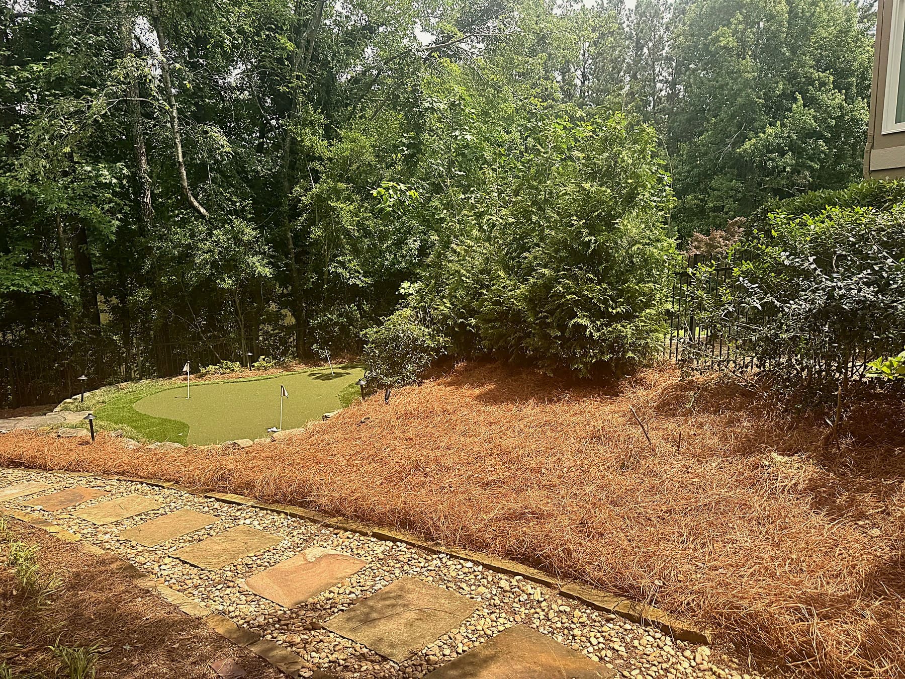 Landscape bed finished with fresh pine straw beside a stone walkway in Johns Creek, GA